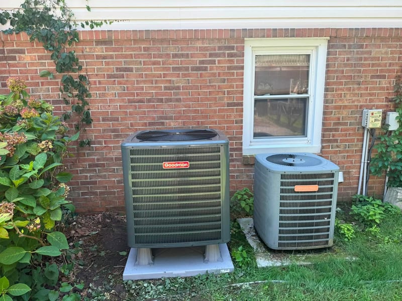 Two outdoor condensers installed side by side beside a brick home