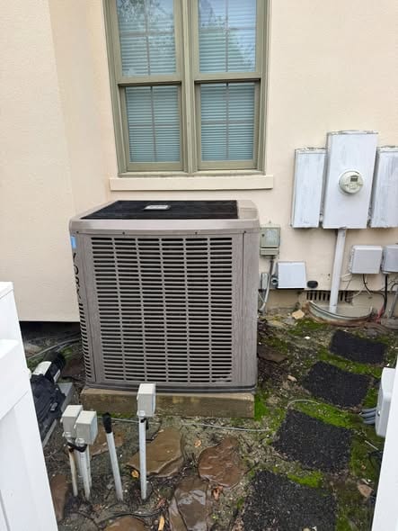 Outdoor AC condenser on a pad beside a stucco wall, with a window above it and electric meters to the right