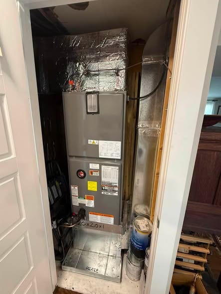 Air handler cabinet in a closet with the door open, foil wrapped duct above it and a drain pan below