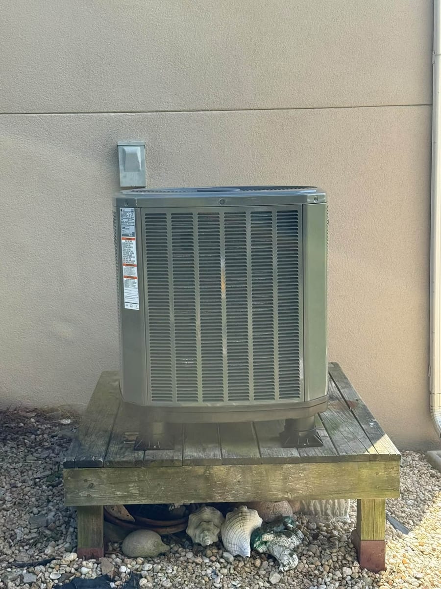 Outdoor unit on a raised wood stand over a gravel bed