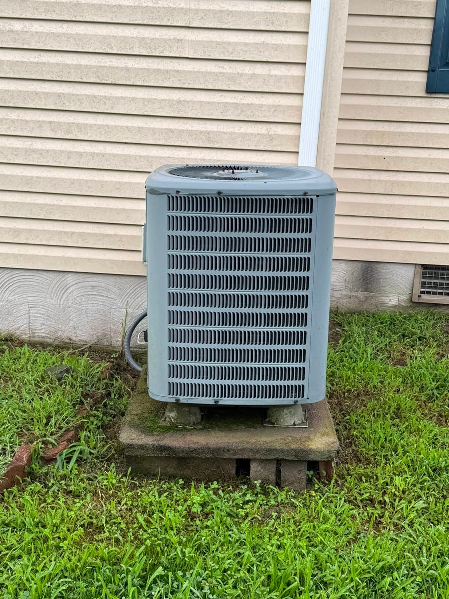 Outdoor condenser on a pad beside tan siding and a green lawn